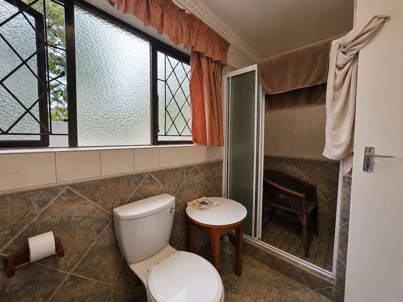 A dated bathroom featuring a toilet, shower enclosure, and tiled finishes, with a large window providing natural light.