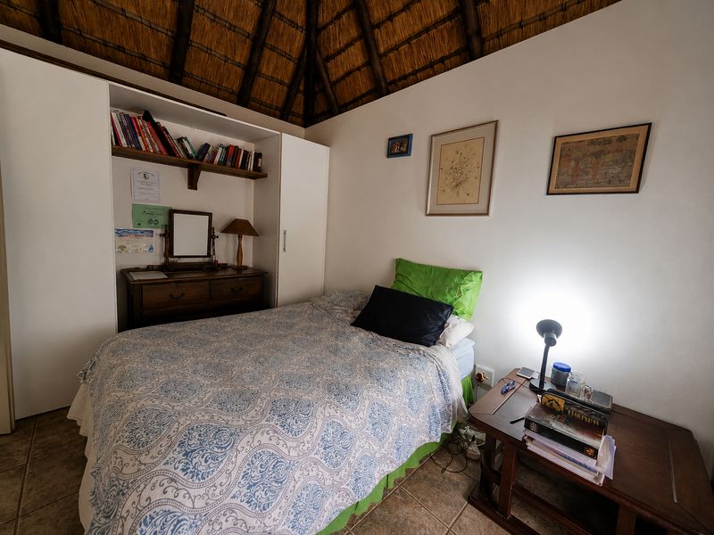 A cozy bedroom featuring a unique thatched roof ceiling, built-in wardrobe storage, and tiled flooring.