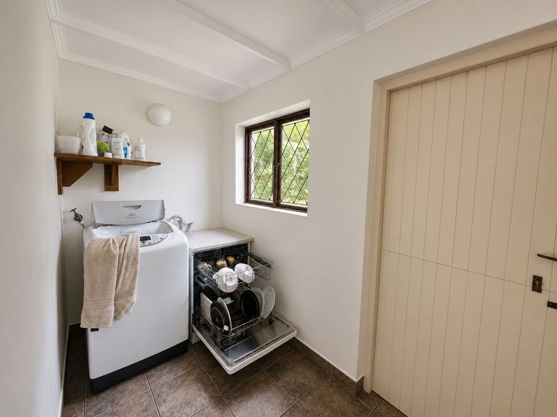 Functional laundry area featuring tiled flooring, a leaded glass window, built-in shelving, and space for a washing machine and integrated dishwasher.