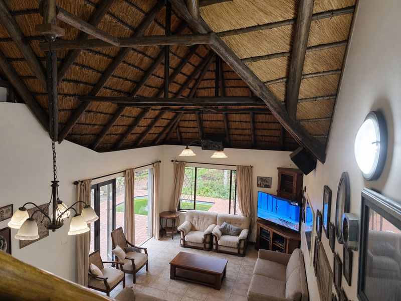 Spacious living room featuring a high vaulted thatched ceiling with exposed timber trusses, tiled floors, and large sliding doors opening to the pool area.