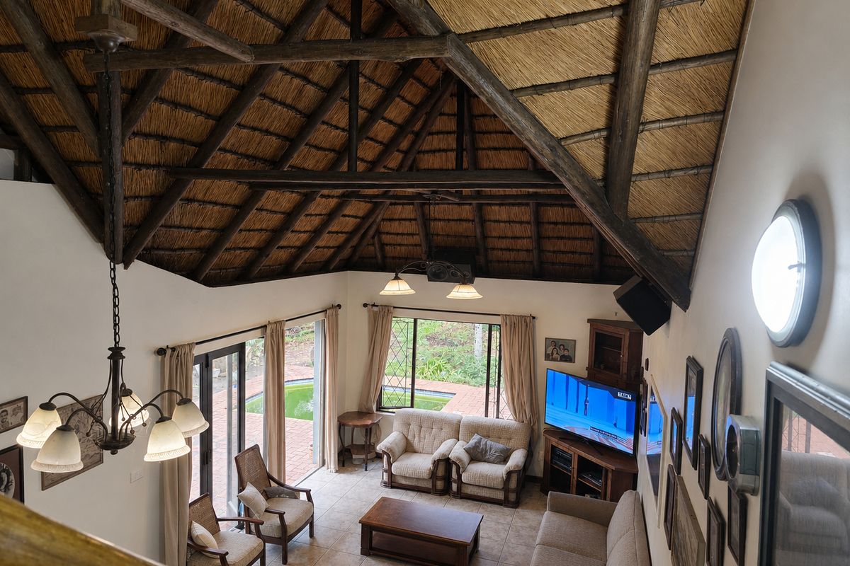 Spacious living room featuring a high vaulted thatched ceiling with exposed timber trusses, tiled floors, and large sliding doors opening to the pool area.