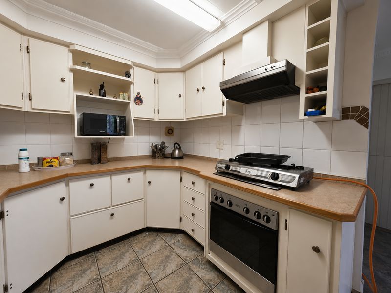 A functional kitchen featuring white built-in cabinetry, laminate countertops, tiled backsplash, and integrated cooking appliances including an oven and gas hob.
