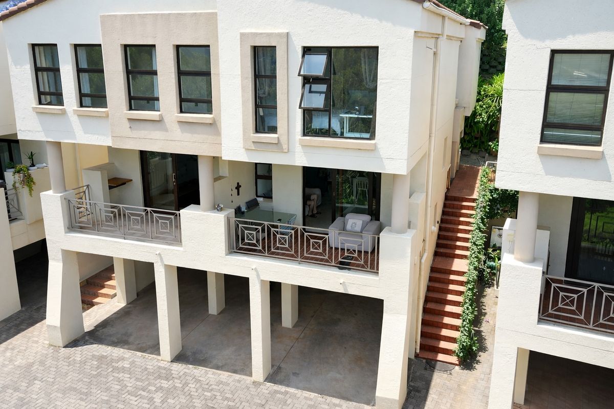 Rear elevation of a multi-level townhouse featuring a covered balcony with metal railings, external staircase, and ground-level covered parking area.