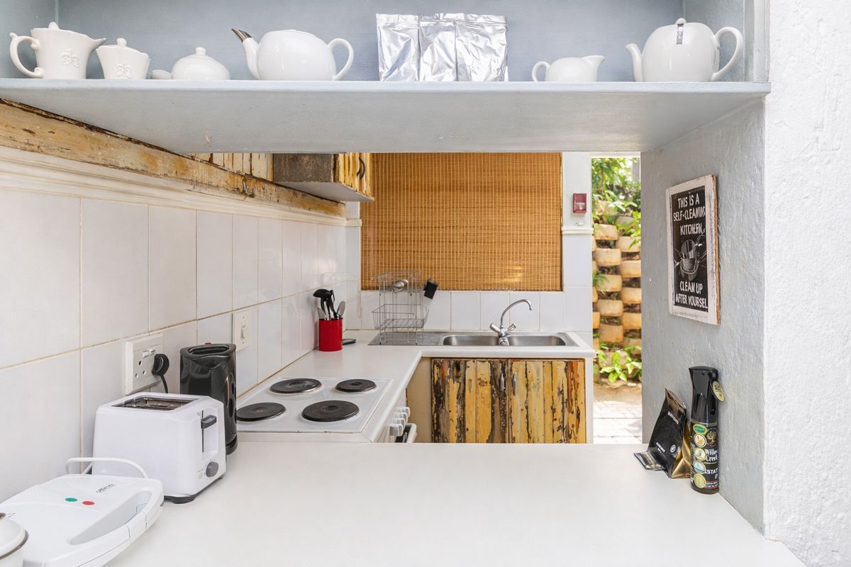 Compact kitchen featuring a built-in hob, oven, and stainless steel sink with tiled splashbacks and open shelving, showing signs of wear on cabinetry.