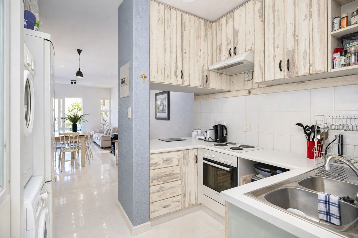 Compact kitchen featuring built-in cabinetry, electric hob, oven, and stainless steel sink, flowing into an open-plan living and dining area.