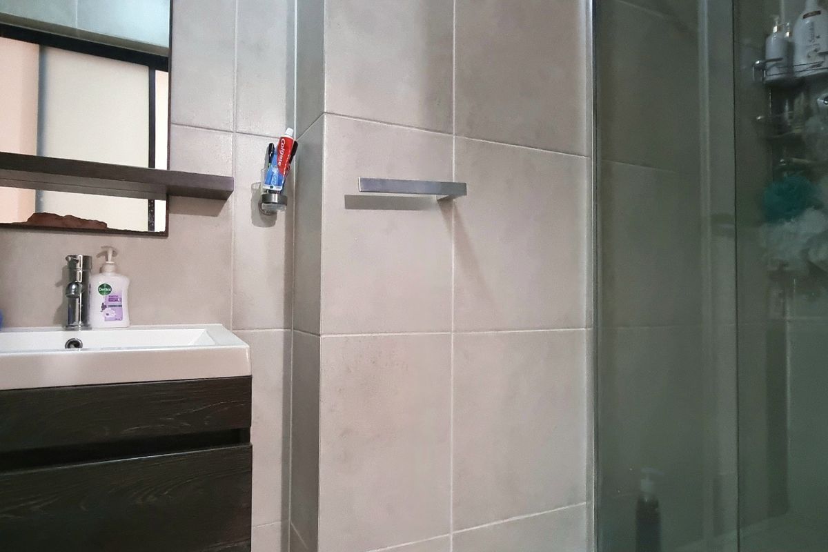A modern bathroom featuring a dark wood vanity cabinet, ceramic basin, wall-mounted mirror, and a glass-enclosed shower with neutral wall tiling.