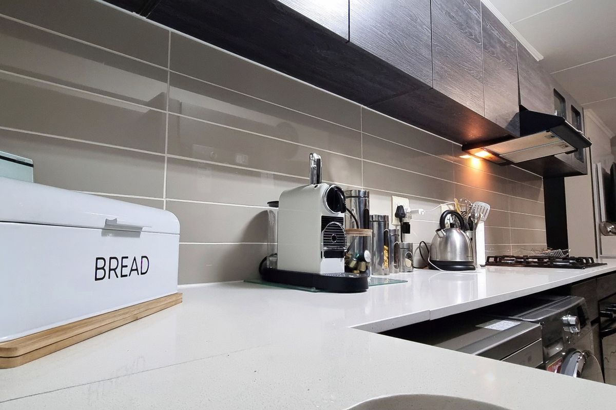 Modern kitchen featuring sleek dark cabinetry, light quartz countertops, and a contemporary subway tile backsplash with integrated cooking appliances.