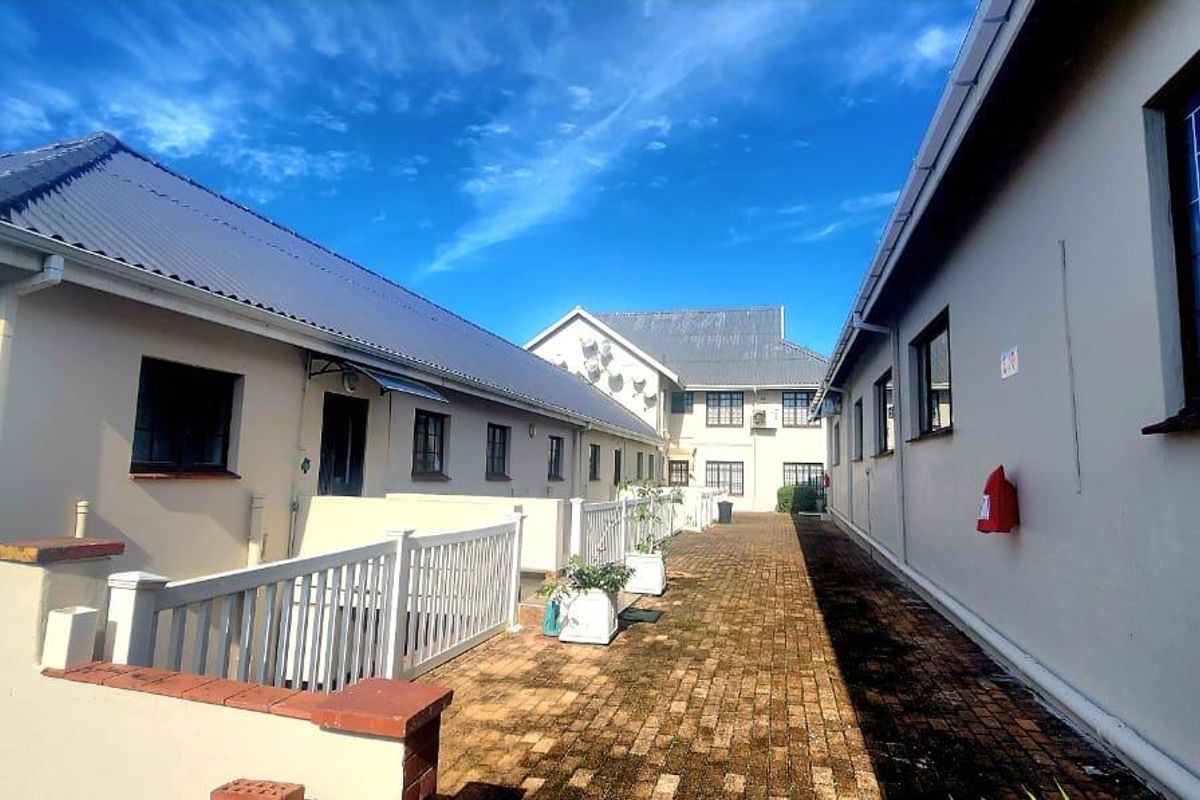 A view of the exterior walkway between apartment building wings, featuring brick paving, security-fitted windows, and metal roofing.