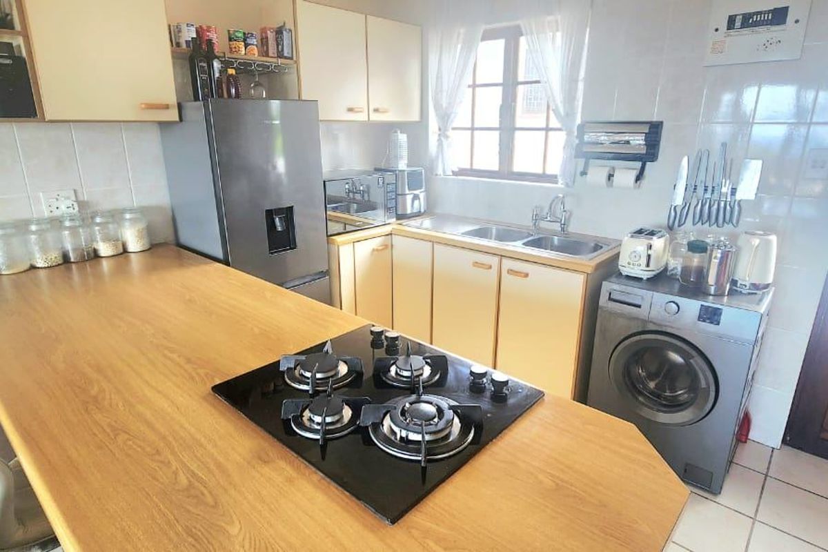 Functional kitchen featuring a gas hob, double sink, tiled splashback, and ample built-in cabinetry with a breakfast bar area.