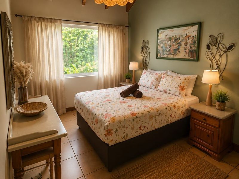 A cozy bedroom featuring a high vaulted ceiling with exposed timber beams, tiled flooring, and a large window providing natural light.