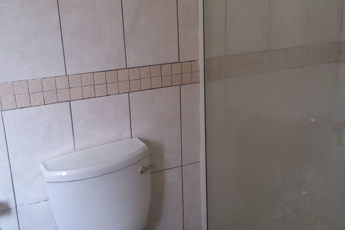 A functional bathroom featuring a standard toilet and a glass-enclosed shower with tiled walls and flooring.