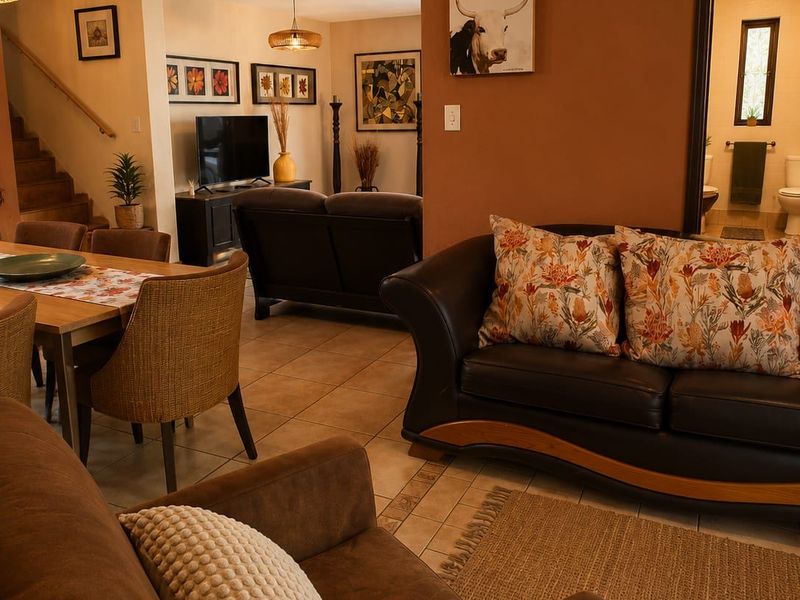 An open-plan living and dining area featuring tiled flooring, a staircase, and warm-toned walls, with an adjacent view into a bathroom.