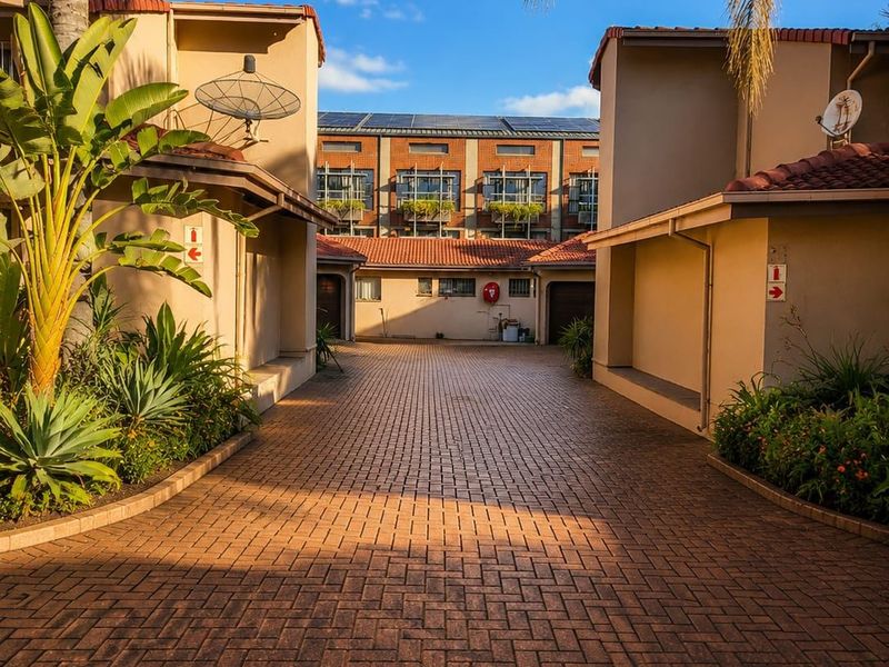 A well-maintained paved driveway leading into a townhouse complex, featuring established landscaping and clear access to residential units.