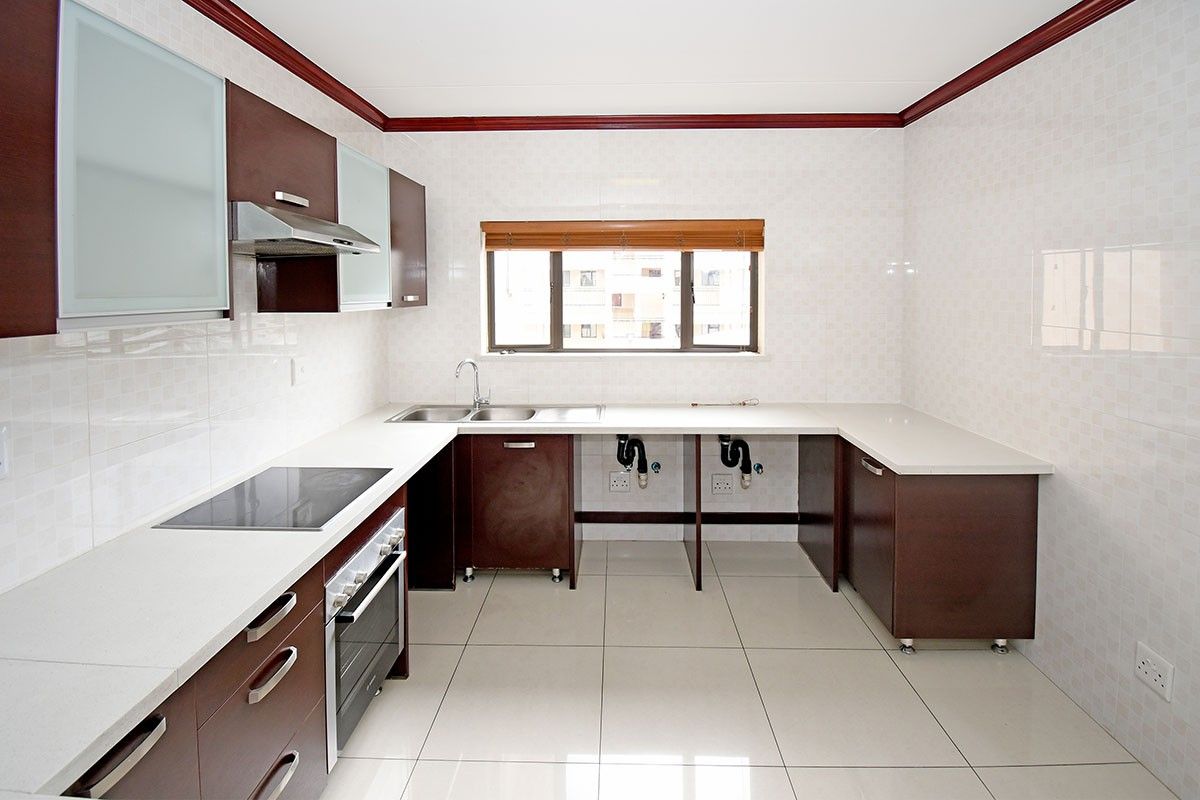 A clean, functional kitchen featuring dark wood cabinetry, white stone countertops, built-in oven, electric hob, and tiled finishes throughout.