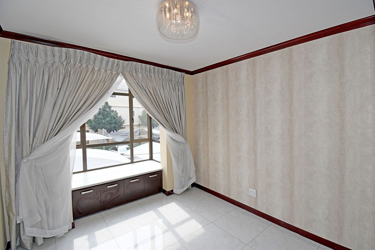 A bright, empty bedroom featuring tiled flooring, crown molding, and a built-in window seat with integrated storage cabinetry.