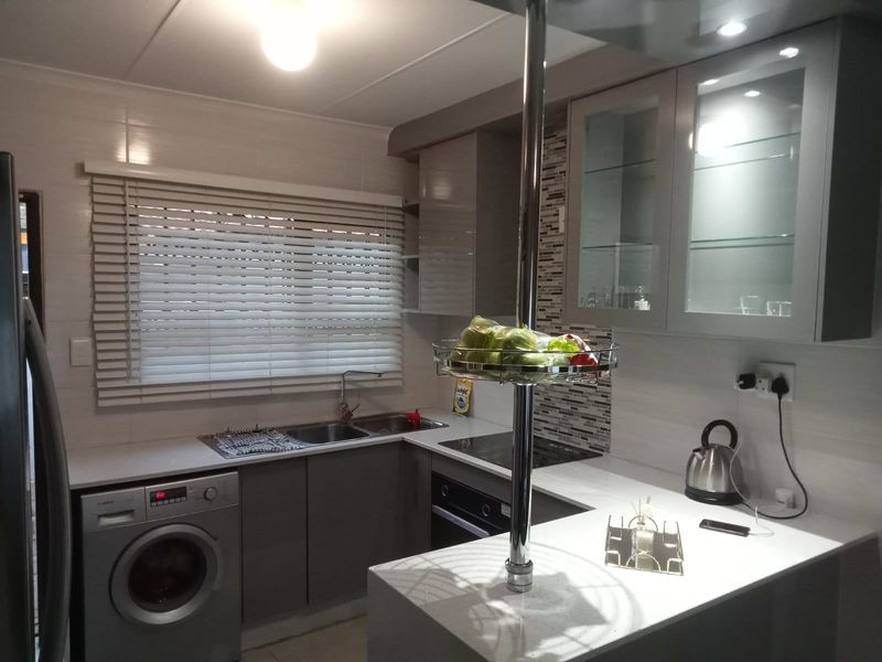 Modern kitchen featuring sleek grey cabinetry, stone countertops, mosaic tile splashback, integrated oven and hob, and a functional double sink setup.