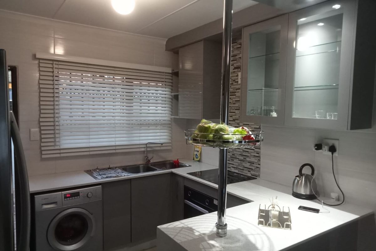 Modern kitchen featuring sleek grey cabinetry, stone countertops, mosaic tile splashback, integrated oven and hob, and a functional double sink setup.