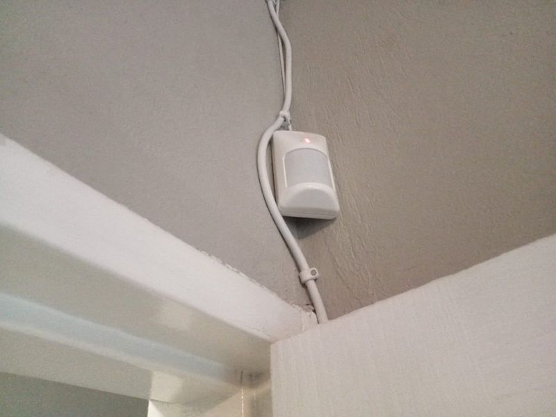 A close-up view of a wall-mounted security motion sensor with visible surface-mounted electrical wiring.