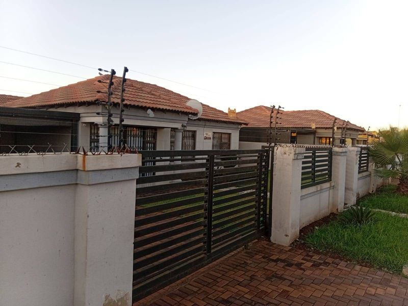 Front exterior view of a residential property featuring a tiled roof, secure perimeter wall with electric fencing, and a metal driveway gate.