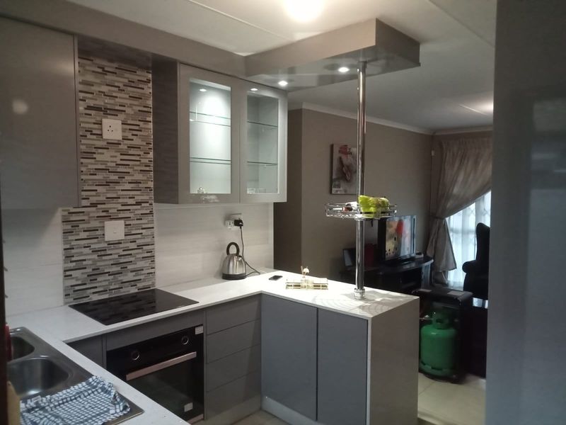 Modern open-plan kitchen featuring grey cabinetry, quartz countertops, mosaic tile backsplash, and integrated appliances, flowing into the adjacent living area.
