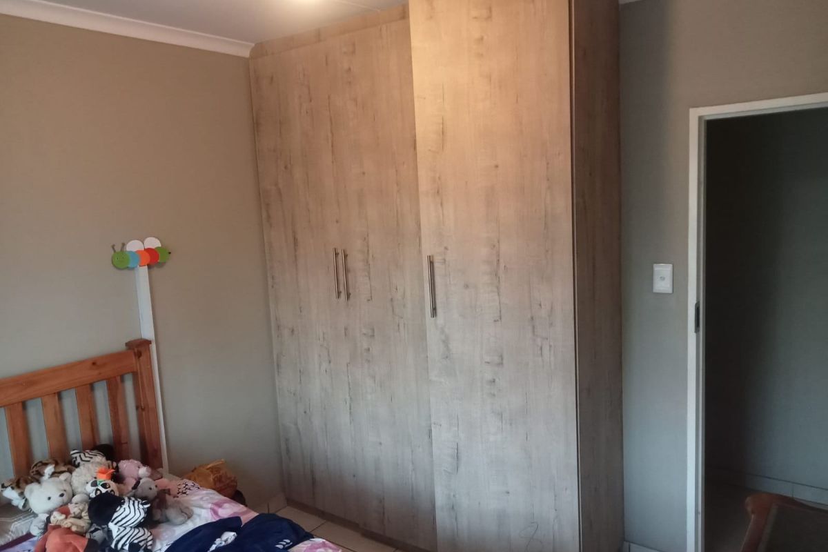 A bedroom featuring a large, modern wood-finish built-in wardrobe and tiled flooring.