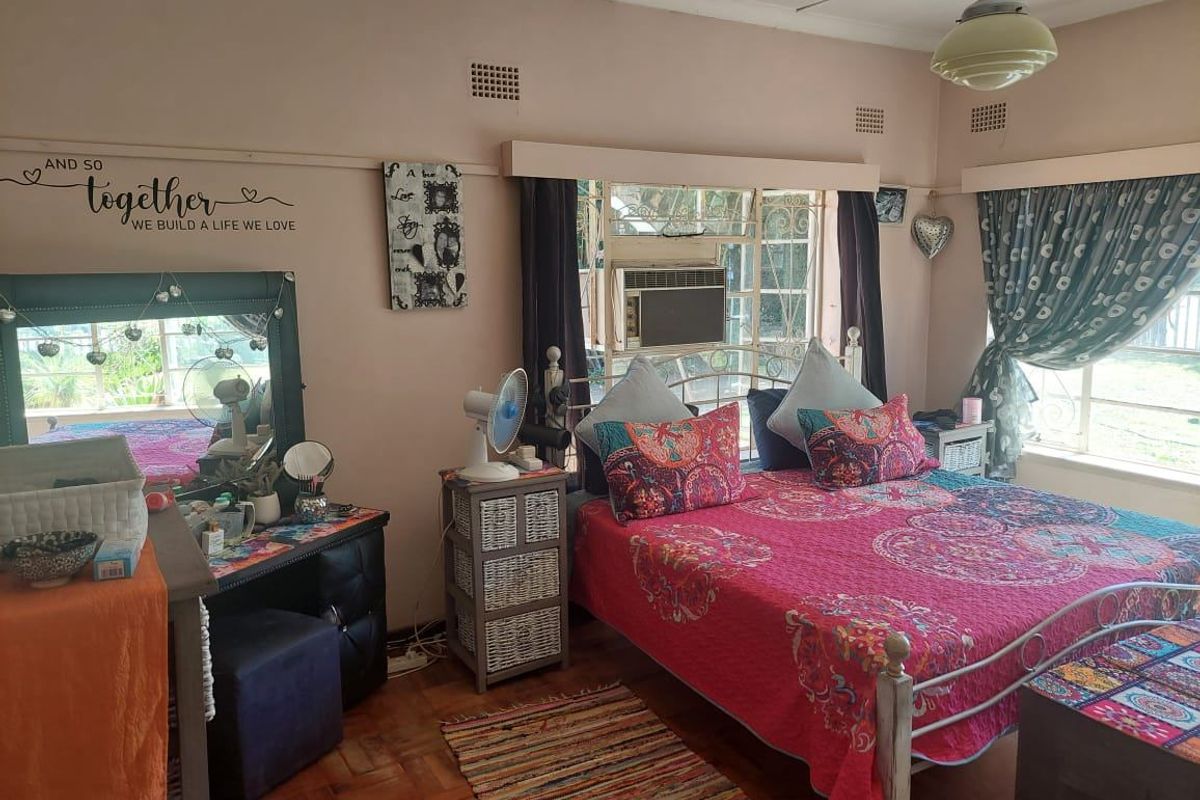 A bedroom featuring parquet flooring, a built-in window air conditioning unit, and steel-framed windows, offering a functional space with potential for modernization.