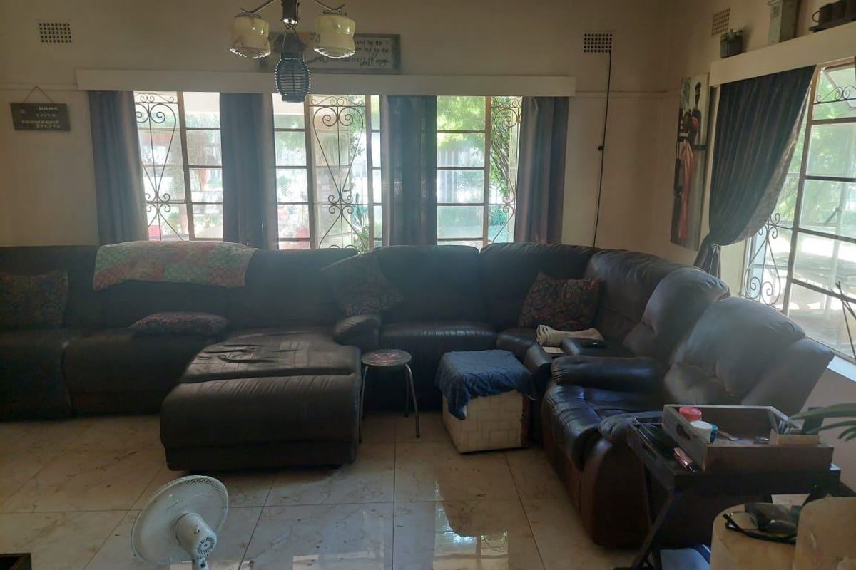 A spacious living room featuring tiled flooring, large windows with security gates, and a central ceiling light fixture.