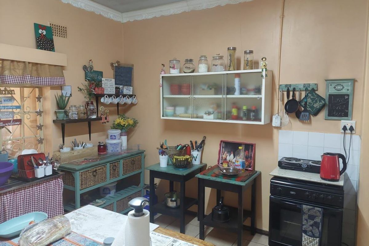 A compact kitchen area featuring a freestanding stove, wall-mounted storage cabinetry, and tiled flooring with decorative ceiling cornicing.