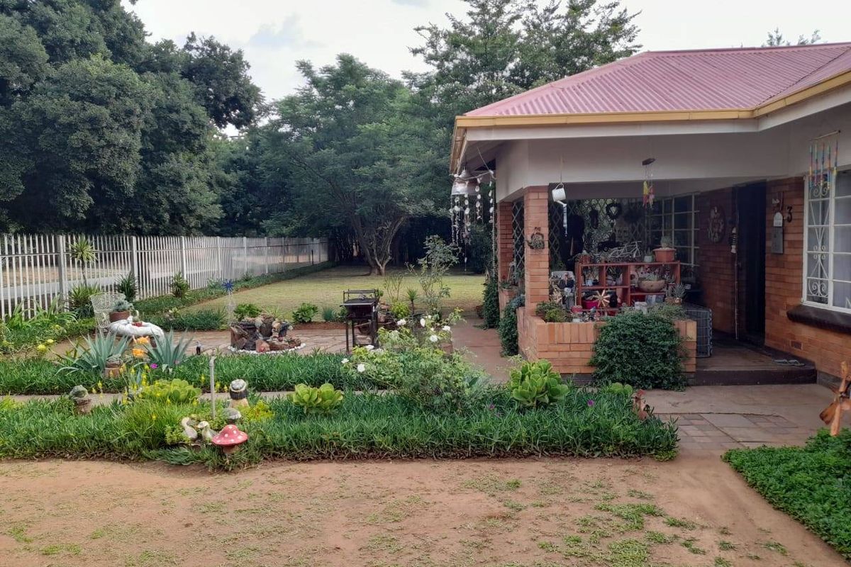A view of the rear garden featuring a covered brick patio, paved outdoor area, and established landscaping with perimeter fencing.