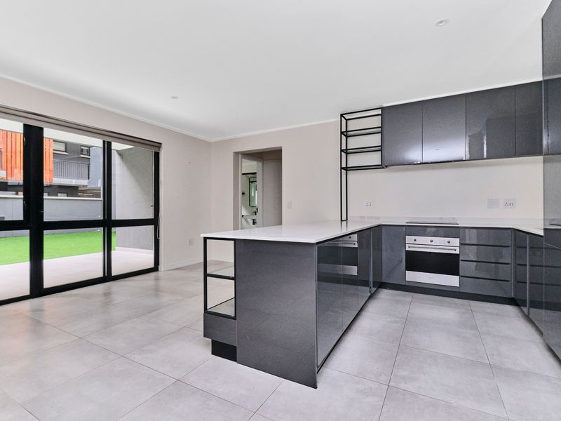 Modern open-plan kitchen featuring sleek grey cabinetry, stone countertops, and integrated appliances, flowing seamlessly to an outdoor patio area.