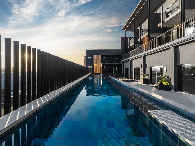 A modern lap pool area featuring dark tiled finishes, a sleek metal privacy screen, and direct access to the apartment building's exterior.
