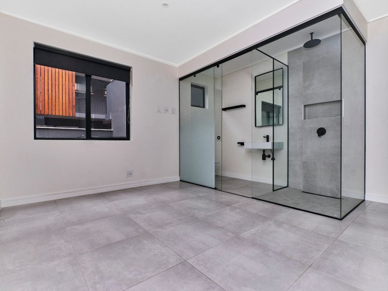 Modern bedroom featuring a sleek, glass-enclosed ensuite bathroom with contemporary black fixtures, large format floor tiles, and a minimalist design aesthetic.