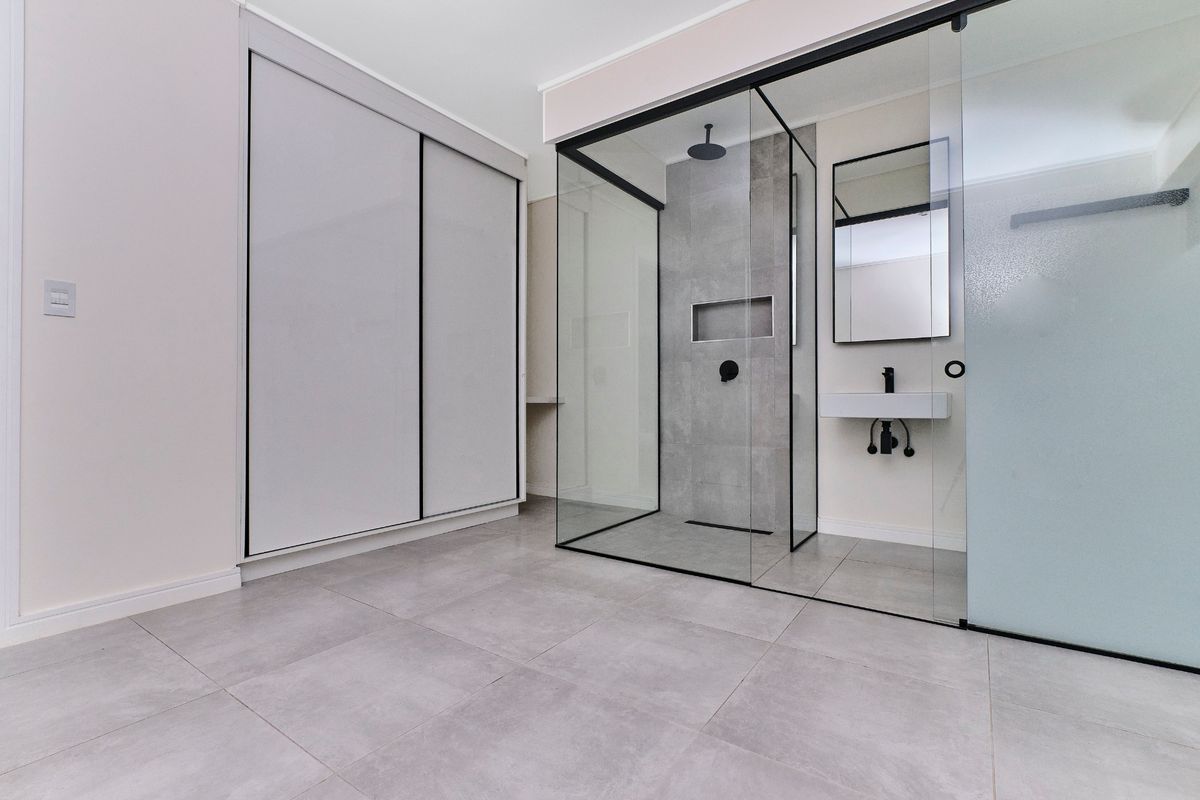 Modern bathroom featuring a walk-in glass shower, wall-mounted basin, and integrated wardrobe storage with contemporary grey tiling throughout.