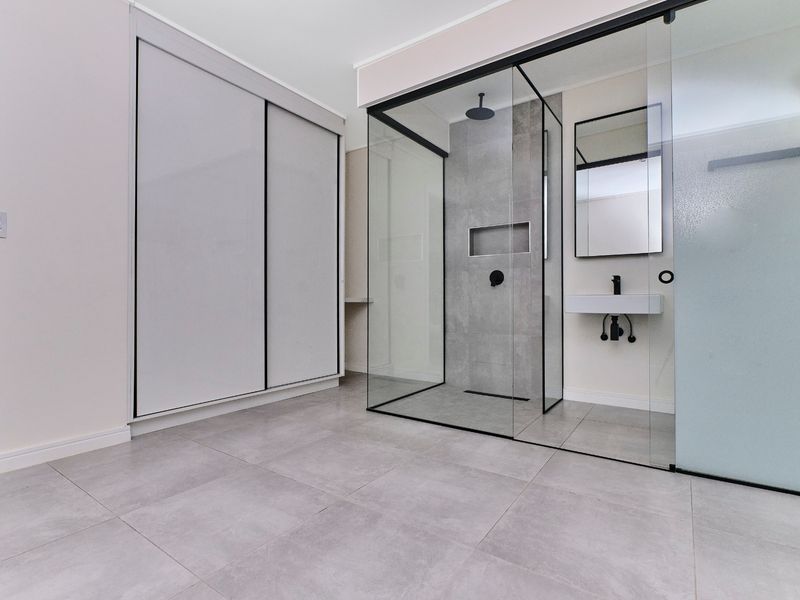 Modern bathroom featuring a walk-in glass shower, wall-mounted basin, and integrated wardrobe storage with contemporary grey tiling throughout.