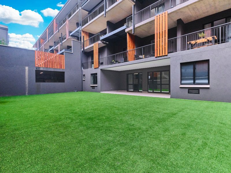 A well-maintained rear courtyard featuring artificial turf, bordered by a modern apartment building with private balconies and timber privacy screens.