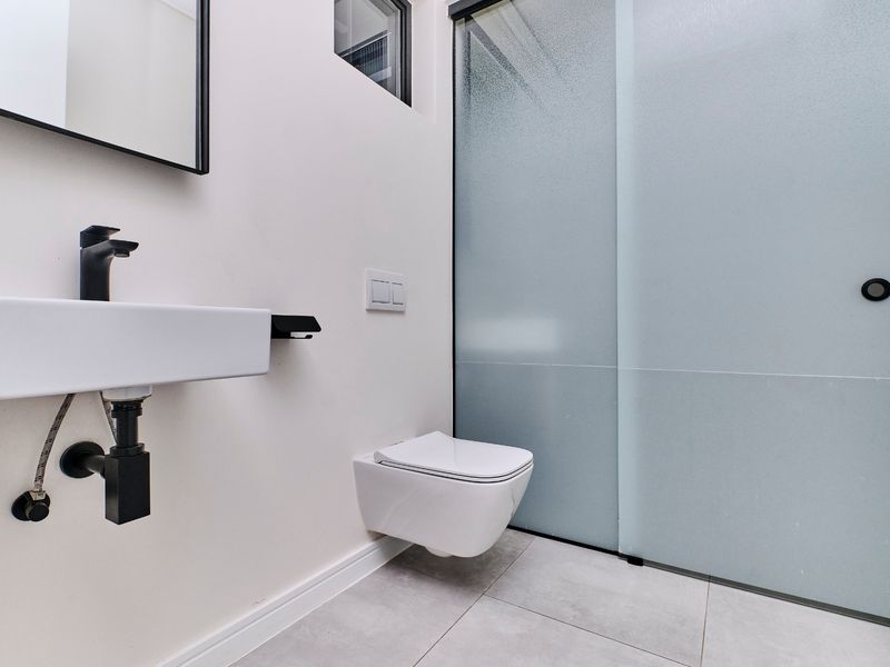 Modern bathroom featuring a wall-mounted basin with black fixtures, a wall-hung toilet, and a sleek frosted glass sliding door.
