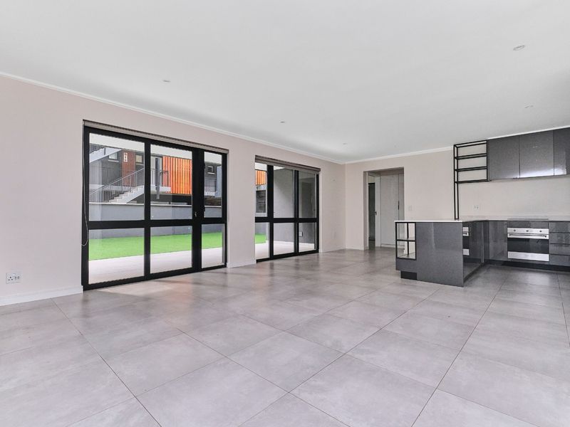 Spacious open-plan living and kitchen area featuring modern grey cabinetry, tiled floors, and large sliding doors providing access to the outdoor space.