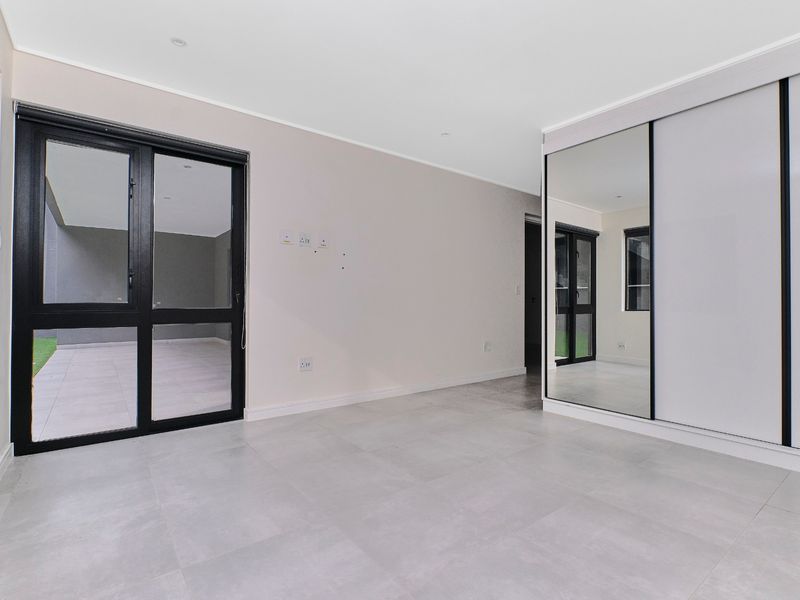 A bright, modern bedroom featuring large format floor tiles, a built-in mirrored sliding wardrobe, and direct access to an outdoor patio area.