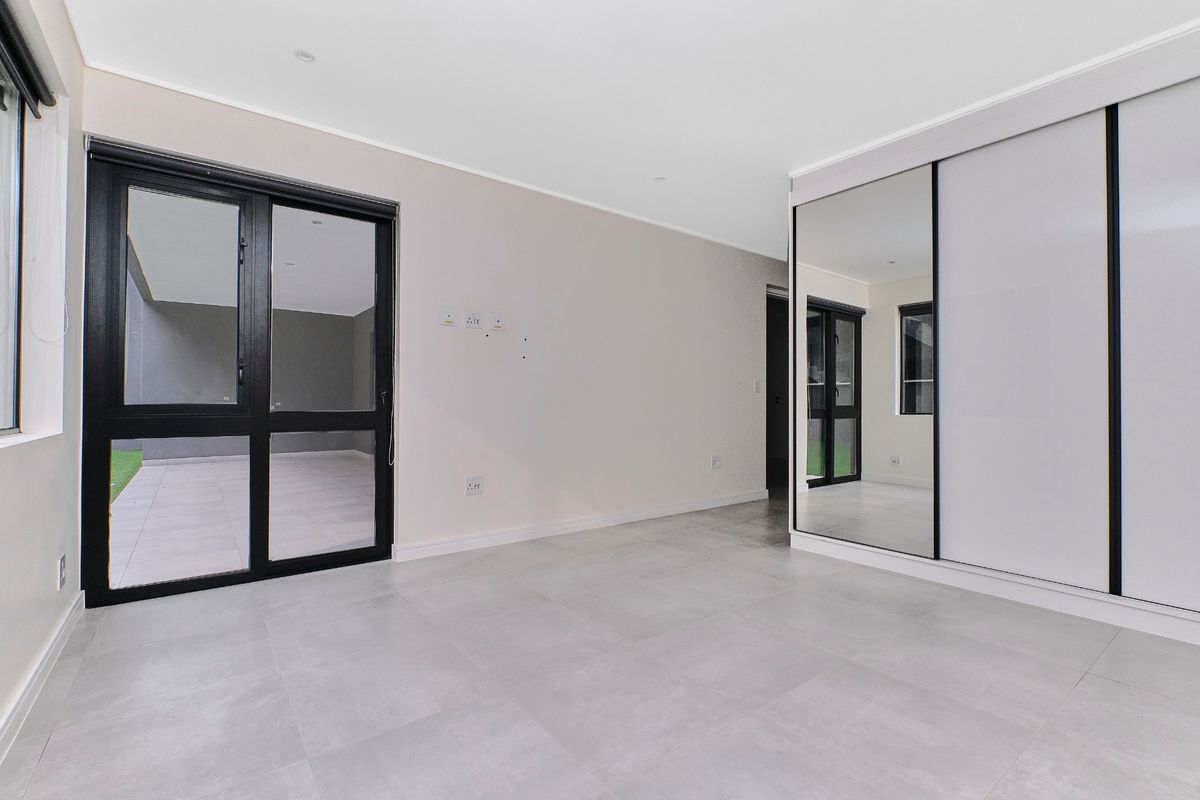 A bright, modern bedroom featuring large format floor tiles, a built-in mirrored sliding wardrobe, and direct access to an outdoor patio area.