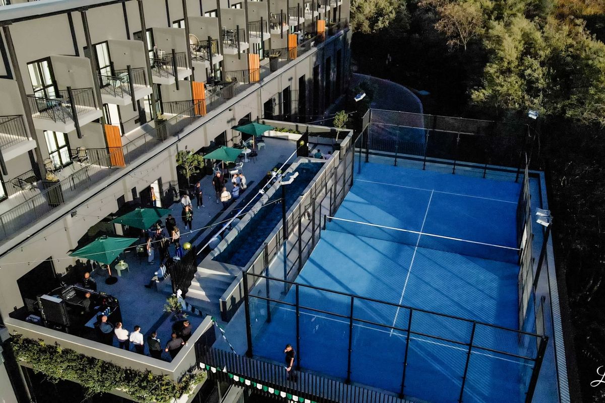 Aerial view of a modern apartment complex featuring a padel court, swimming pool, and private balconies for residents.
