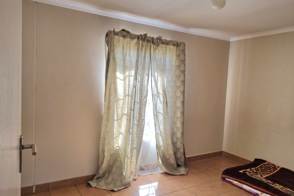 A simple, empty bedroom featuring neutral walls, tiled flooring, and a window with curtains.