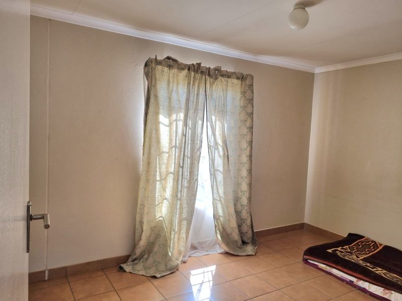 A simple, empty bedroom featuring neutral walls, tiled flooring, and a window with curtains.