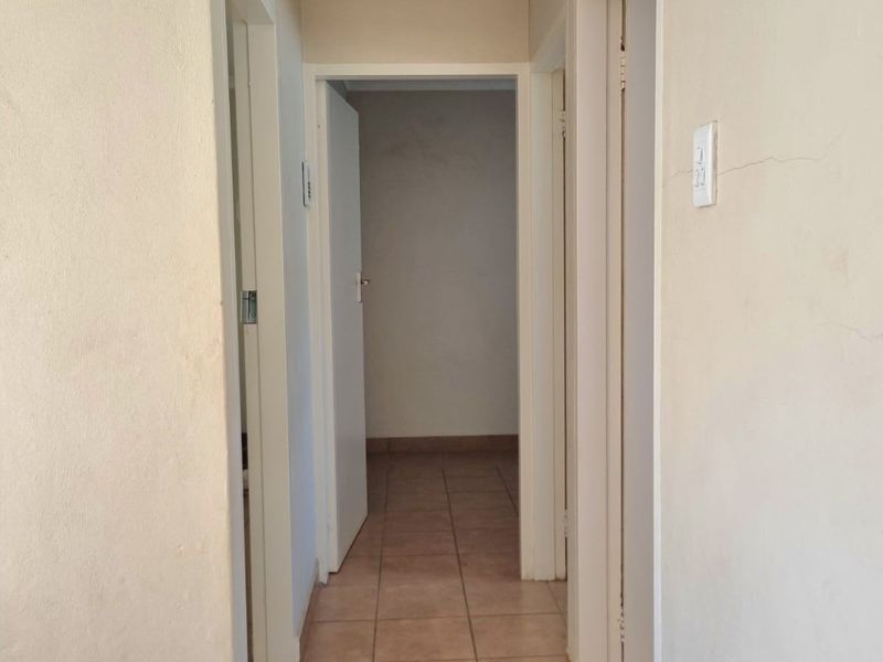 A functional hallway featuring tiled flooring, coved cornicing, and a ceiling access hatch, providing access to multiple rooms.
