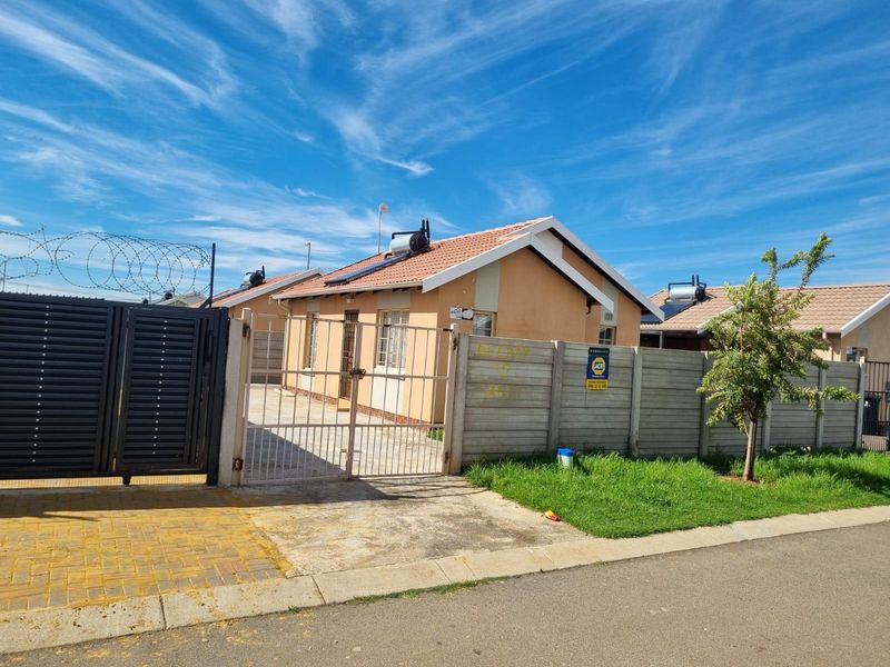 Front exterior view of a single-story house featuring a tiled roof, solar geyser, paved driveway, and a secure boundary wall with razor wire.