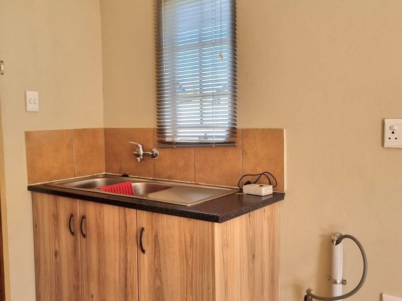 A functional laundry area featuring a stainless steel sink, laminate cabinetry, tiled splashback, and dedicated plumbing connections for a washing machine.