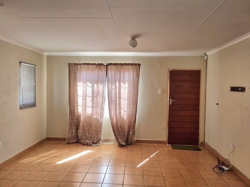An empty living room featuring tiled flooring, a timber entrance door, and coved ceilings, offering a blank canvas for interior design.