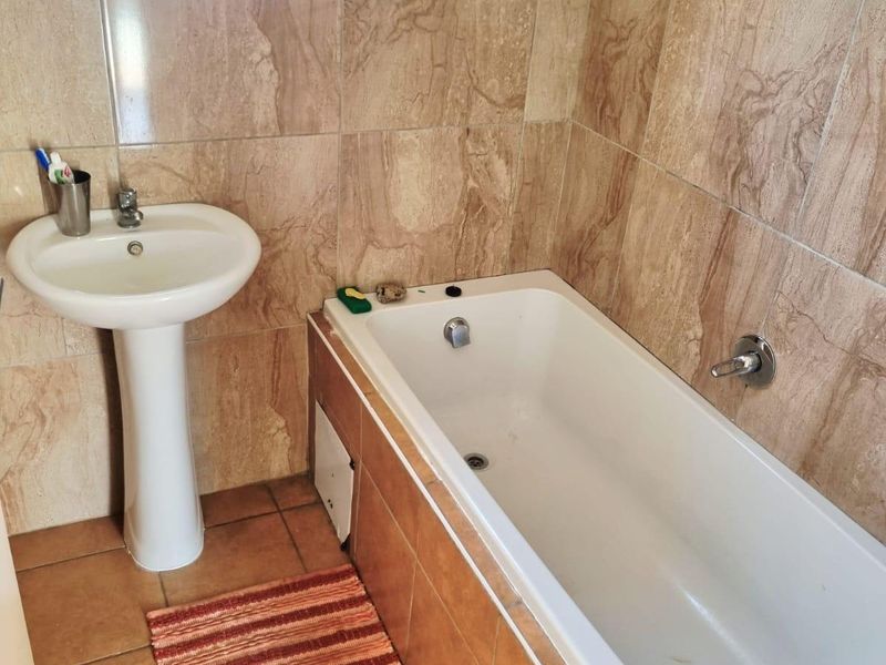 A functional bathroom featuring a pedestal basin, built-in bathtub, and full-height wall tiling.