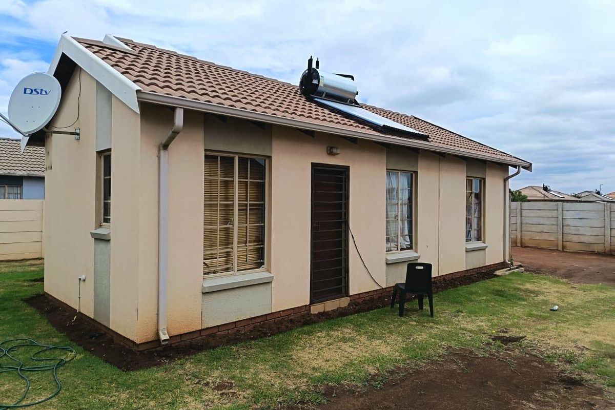 Rear view of a single-story residential house featuring a tiled roof, solar water heating system, and security gate access.