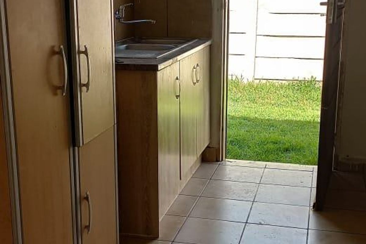 A compact kitchen area featuring built-in cabinetry, a stainless steel sink, and tiled flooring, with direct access to the rear garden.