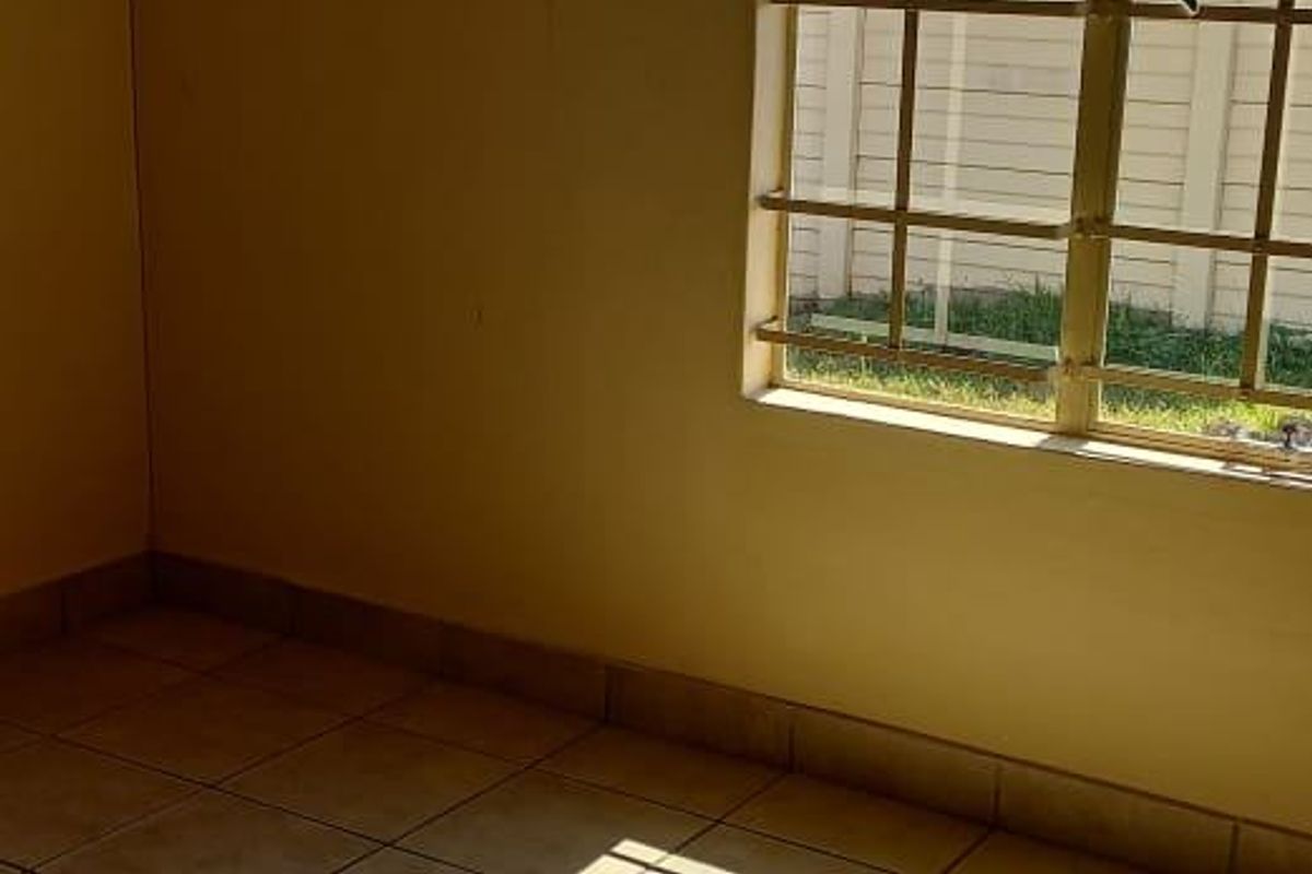 An empty bedroom featuring neutral tiled flooring and a window fitted with security bars, offering a blank canvas for personalization.